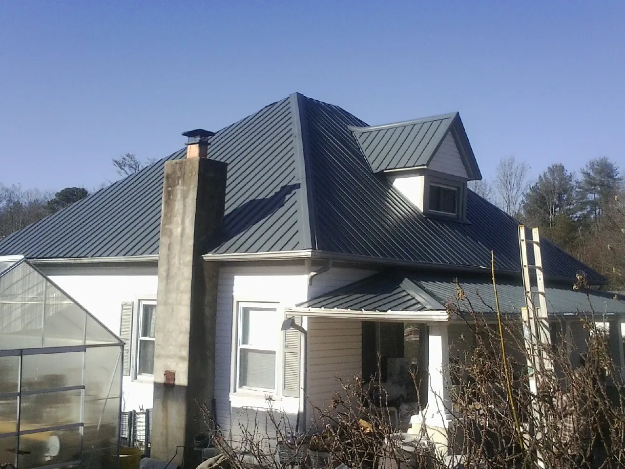 Dark blue standing seam metal roof on a white farmhouse with dormer — Slate & Tile Roof Repair by Roofing Brothers in Deshler
