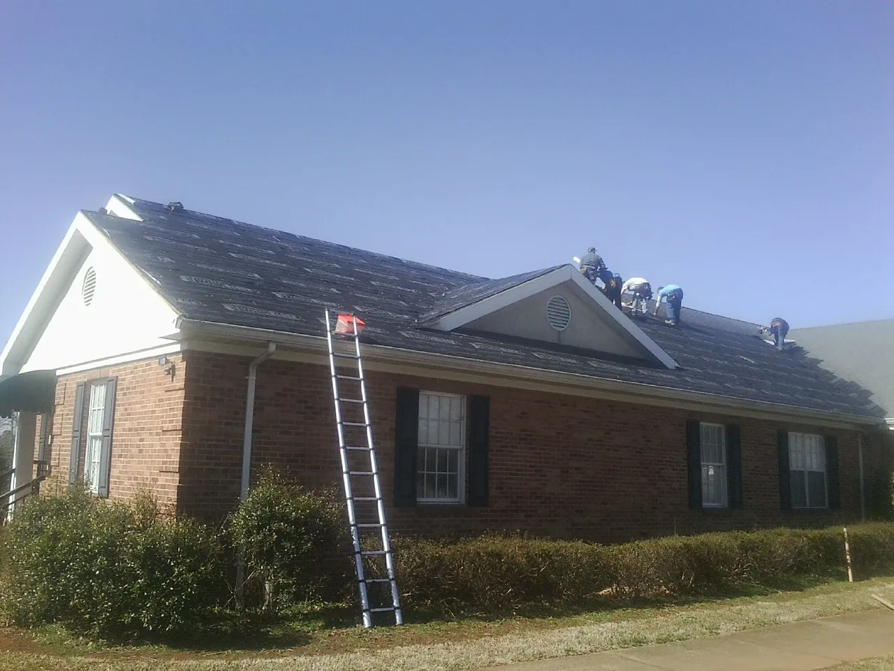 Crew tearing shingles off a brick ranch roof with a ladder set — Emergency Roof Repair work by our crew in Deshler