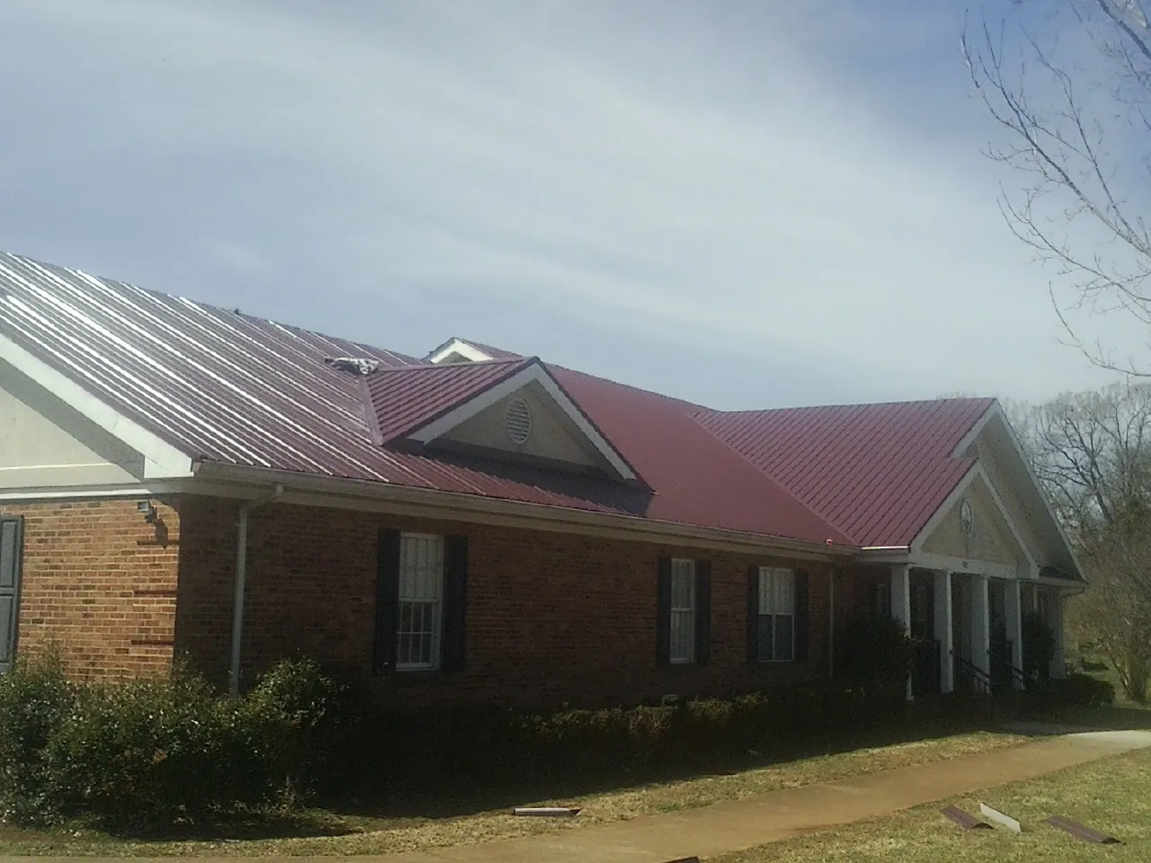 Red metal roof with gabled entries on a long brick building, from a Hail Damage Roof Repair job in Deshler