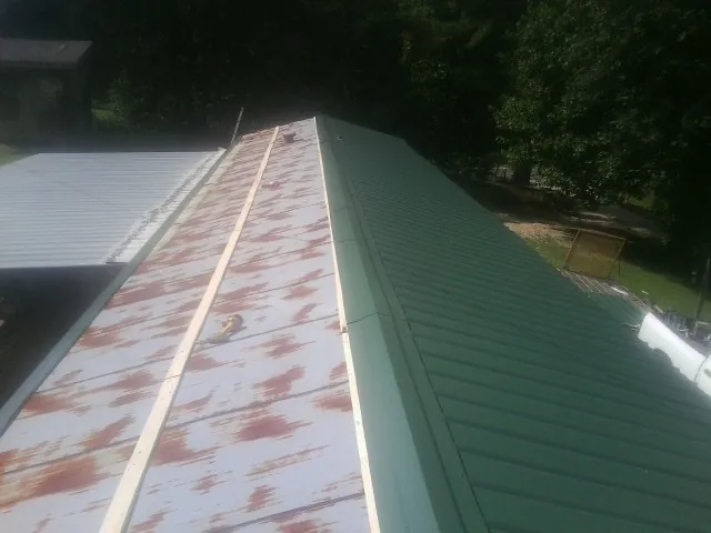 Old rusted panels beside newly installed green metal roofing — Wind Damage Roof Repair by Roofing Brothers in Deshler