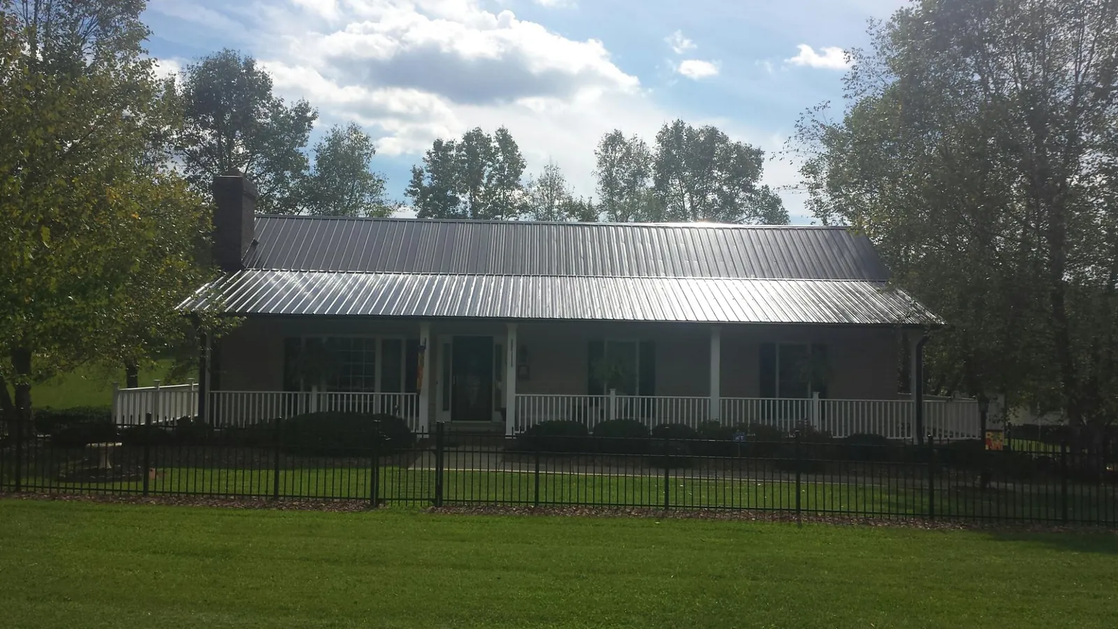 Gray metal roof on a brick ranch with a full width front porch — Gutter Guard Installation work by our crew in Deshler