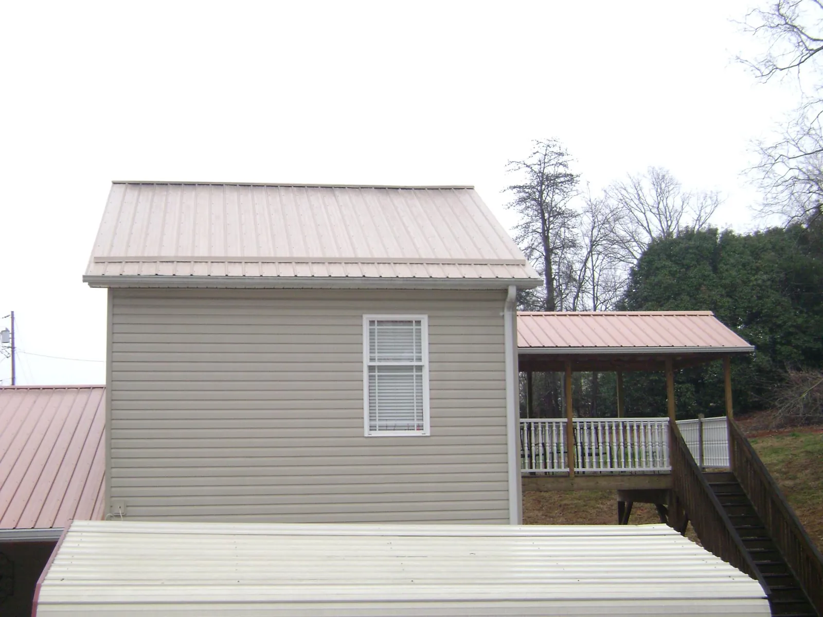 Tan metal roofs on a two story addition and attached porch, from a Roof Replacement job in Deshler